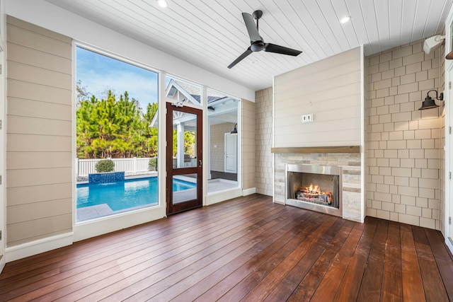 unfurnished living room featuring a warm lit fireplace, wood ceiling, a ceiling fan, and wood finished floors