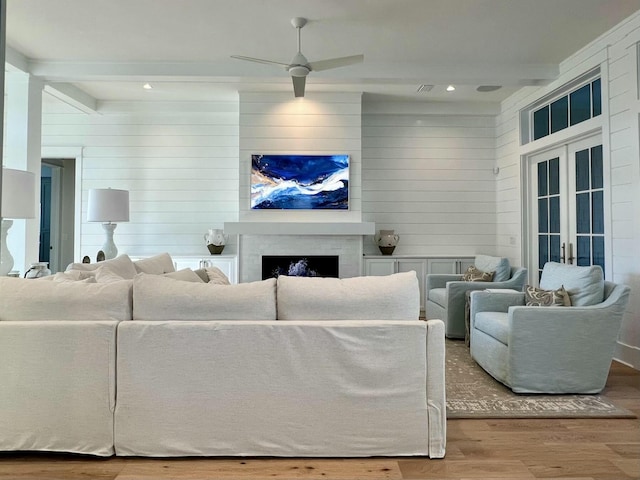 living room with a fireplace, a ceiling fan, beamed ceiling, and wood finished floors