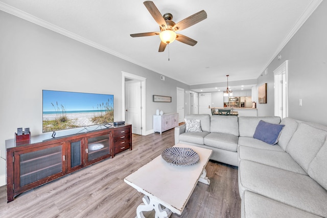 living room featuring ornamental molding, ceiling fan with notable chandelier, and light hardwood / wood-style flooring