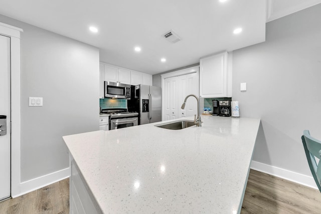 kitchen with sink, stainless steel appliances, tasteful backsplash, light stone countertops, and white cabinets