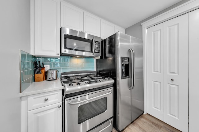 kitchen with white cabinetry, appliances with stainless steel finishes, light stone countertops, light hardwood / wood-style floors, and backsplash