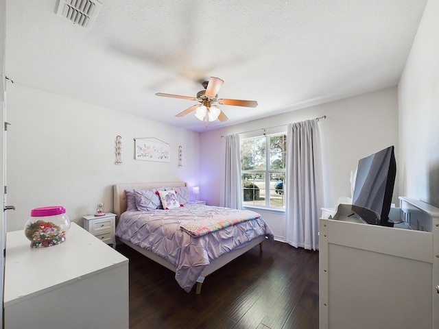 bedroom featuring a textured ceiling, dark wood-style flooring, visible vents, and a ceiling fan