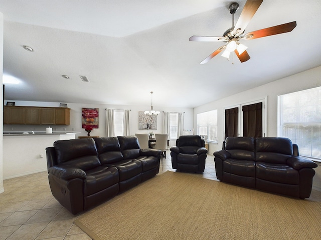 living room featuring light tile patterned flooring, vaulted ceiling, visible vents, and ceiling fan with notable chandelier