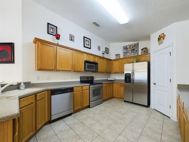 kitchen featuring a textured ceiling, stainless steel appliances, a sink, visible vents, and brown cabinets