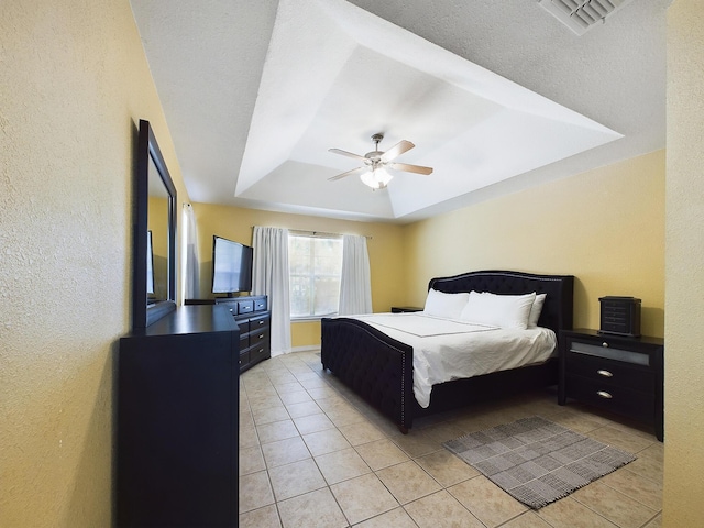 bedroom with light tile patterned floors, a textured wall, visible vents, a ceiling fan, and a raised ceiling