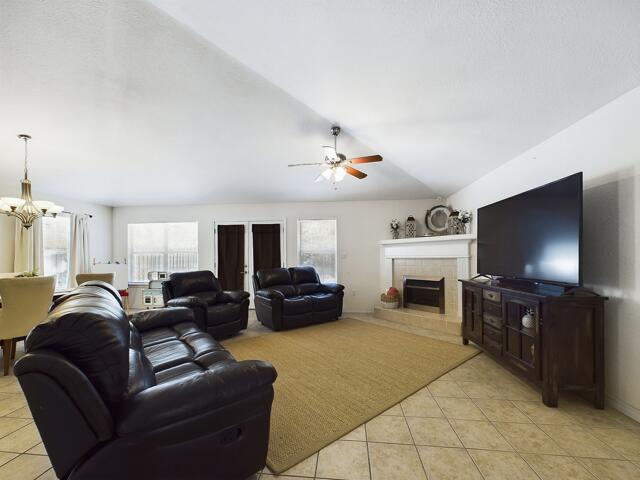 living room featuring light tile patterned floors, a tiled fireplace, and ceiling fan with notable chandelier