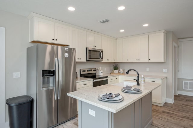 kitchen with sink, a center island with sink, appliances with stainless steel finishes, light stone countertops, and white cabinets