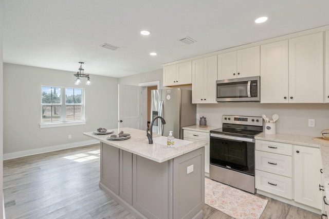 kitchen featuring sink, a kitchen island with sink, white cabinetry, stainless steel appliances, and light stone countertops