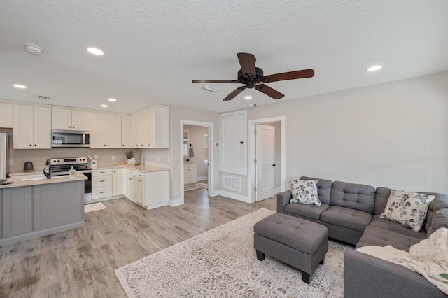 living room with ceiling fan, a textured ceiling, and light wood-type flooring