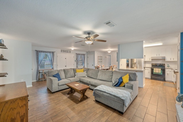 living room featuring ceiling fan, a textured ceiling, and light wood-type flooring