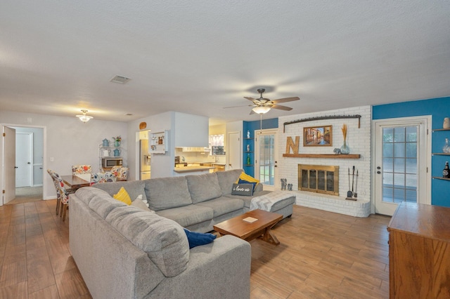 living room with a brick fireplace, a textured ceiling, and light wood-type flooring