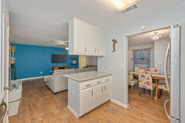 kitchen with stainless steel refrigerator, white cabinetry, kitchen peninsula, and light wood-type flooring