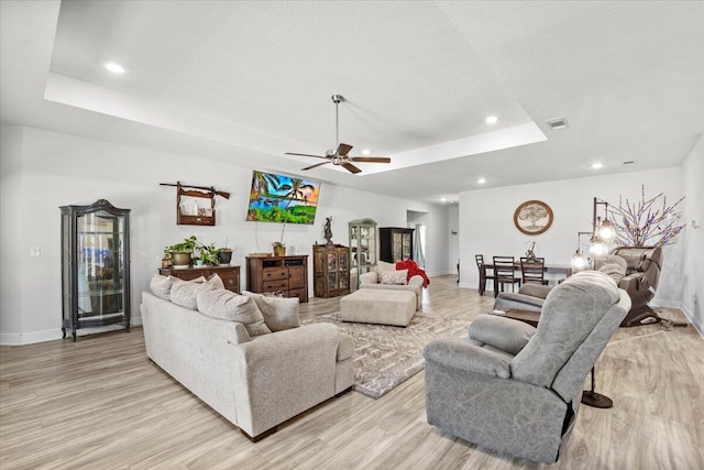 living room with light hardwood / wood-style flooring, a textured ceiling, ceiling fan, and a tray ceiling