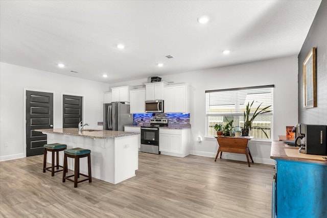 kitchen featuring a breakfast bar area, white cabinets, a kitchen island with sink, stainless steel appliances, and light hardwood / wood-style flooring