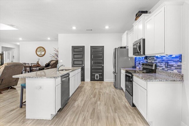 kitchen with white cabinetry, a kitchen island with sink, light stone countertops, and appliances with stainless steel finishes