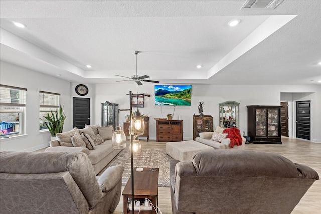 living room with ceiling fan, a tray ceiling, light hardwood / wood-style flooring, and a textured ceiling