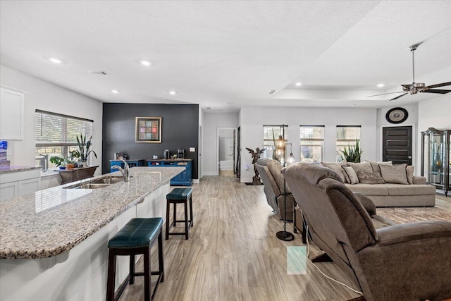 living room featuring ceiling fan, sink, light hardwood / wood-style flooring, and a textured ceiling