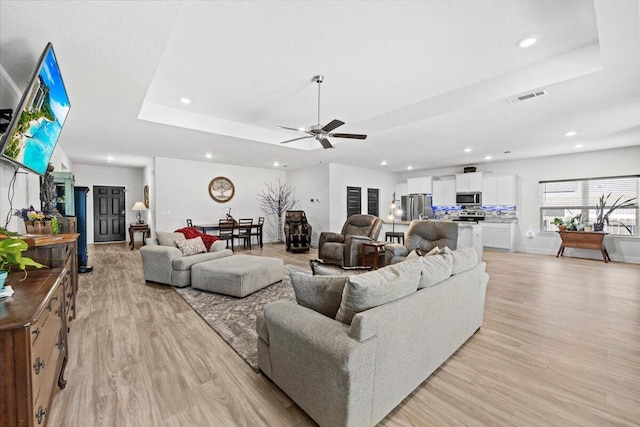 living room with a raised ceiling, ceiling fan, and light hardwood / wood-style floors