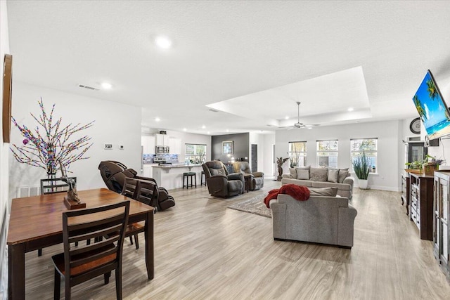 living room featuring a raised ceiling, ceiling fan, and light wood-type flooring