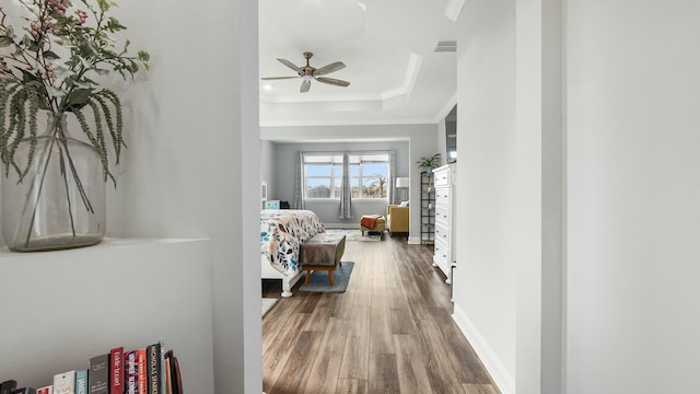 bedroom featuring a tray ceiling, ornamental molding, wood-type flooring, and ceiling fan