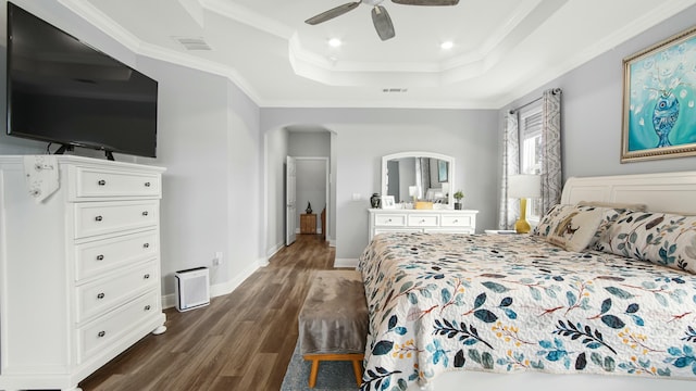 bedroom with ornamental molding, dark wood-type flooring, ceiling fan, and a tray ceiling