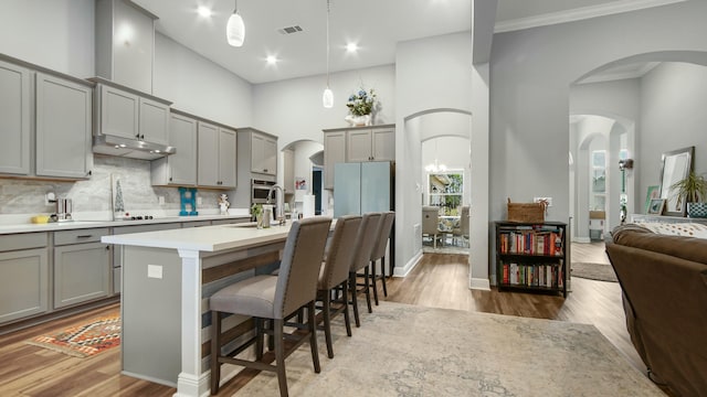 kitchen with a kitchen bar, a kitchen island with sink, gray cabinets, hanging light fixtures, and a high ceiling