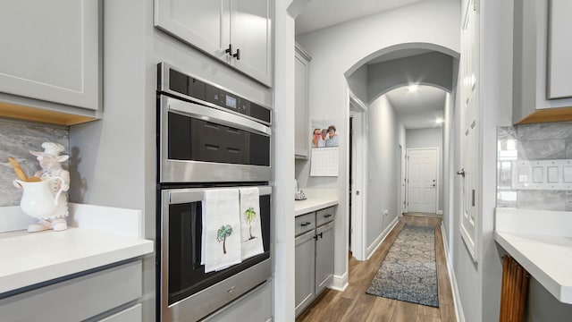 kitchen featuring tasteful backsplash, gray cabinetry, double oven, and wood-type flooring