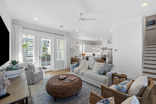 living room featuring ornamental molding, ceiling fan with notable chandelier, and light hardwood / wood-style floors