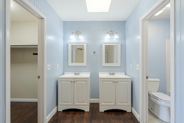 bathroom with baseboards, toilet, two vanities, wood finished floors, and a sink