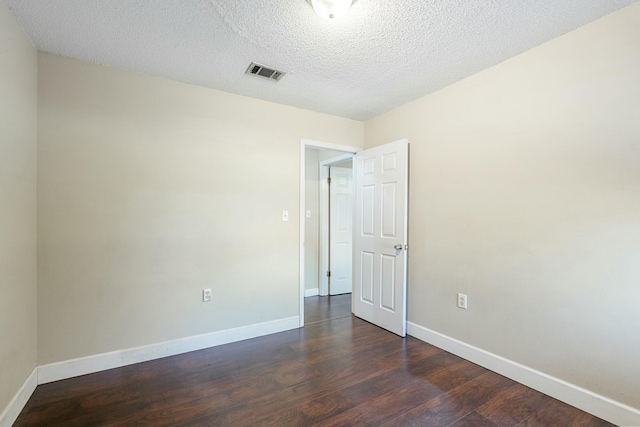 spare room featuring visible vents, dark wood finished floors, a textured ceiling, and baseboards