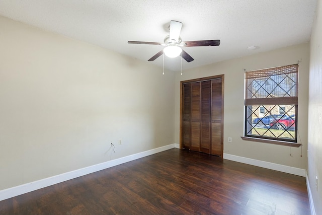 unfurnished bedroom with dark wood-style floors, a closet, ceiling fan, a textured ceiling, and baseboards