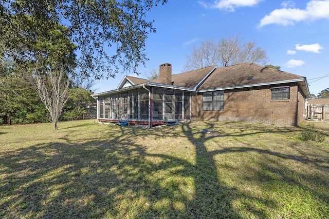 back of property with a lawn, a sunroom, a chimney, fence, and brick siding