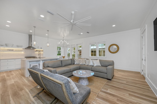 living room with sink, crown molding, light hardwood / wood-style flooring, and a chandelier