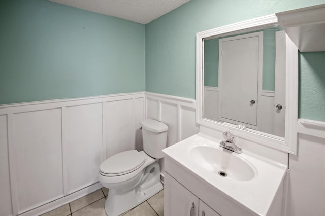 half bath featuring wainscoting, toilet, tile patterned floors, a textured ceiling, and vanity