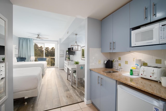 kitchen featuring sink, backsplash, white microwave, light stone counters, and blue cabinets