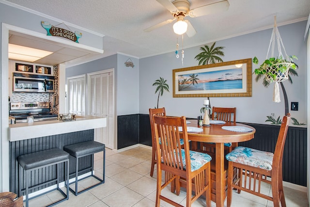 tiled dining area with ceiling fan, ornamental molding, and a textured ceiling