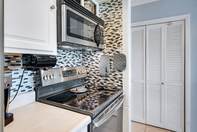 kitchen with appliances with stainless steel finishes, light tile patterned floors, white cabinets, and decorative backsplash