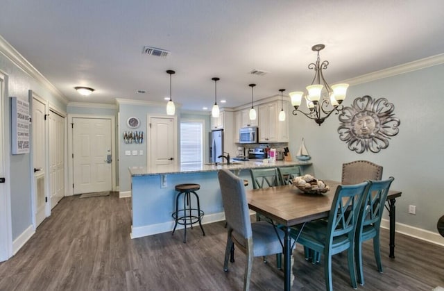 dining area featuring a notable chandelier, dark wood-type flooring, ornamental molding, and sink