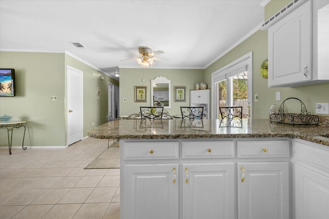 kitchen with crown molding, dark stone countertops, white cabinets, light tile patterned flooring, and kitchen peninsula