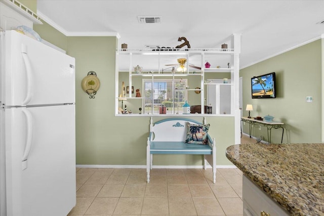 kitchen with light tile patterned floors, crown molding, white cabinetry, white refrigerator, and stone countertops