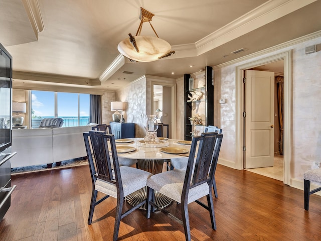 dining room with dark wood-type flooring, a tray ceiling, and crown molding