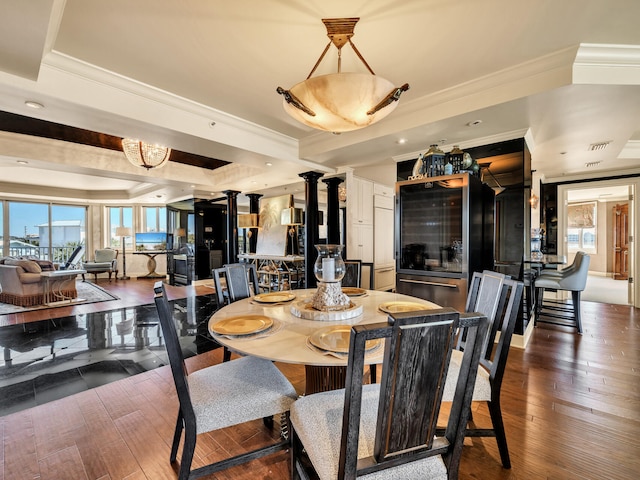 dining area featuring crown molding, dark wood-type flooring, a raised ceiling, and ornate columns