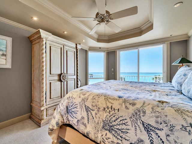 carpeted bedroom featuring a water view, a tray ceiling, access to exterior, and multiple windows