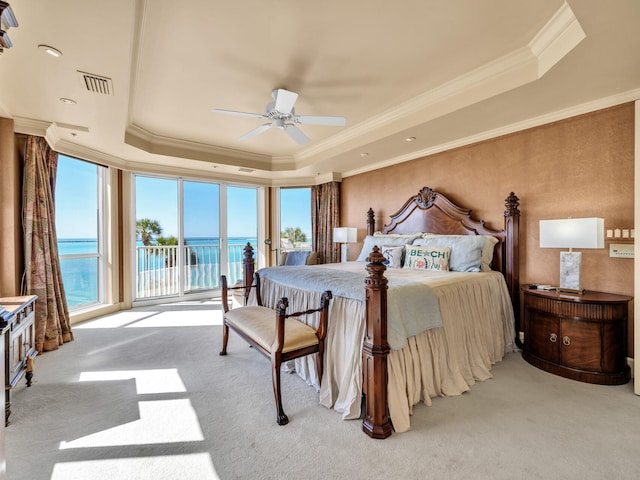 carpeted bedroom with ceiling fan, access to exterior, a water view, a tray ceiling, and ornamental molding