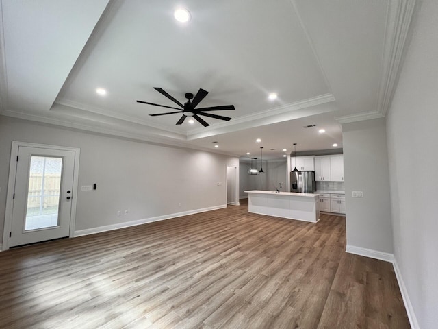 unfurnished living room with a ceiling fan, baseboards, a tray ceiling, and wood finished floors