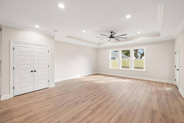 empty room with a raised ceiling, crown molding, light wood-type flooring, and ceiling fan