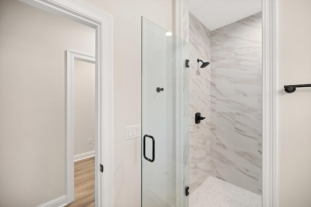 full bath with a marble finish shower, baseboards, and wood finished floors