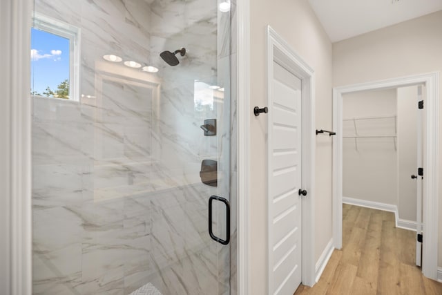 bathroom featuring a walk in closet, baseboards, a marble finish shower, and wood finished floors