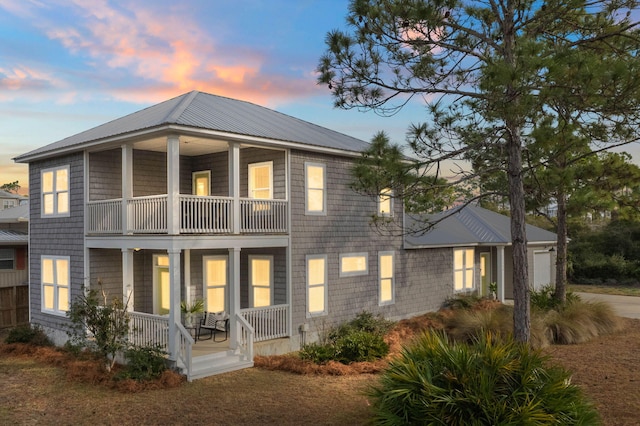 back house at dusk with a balcony and covered porch