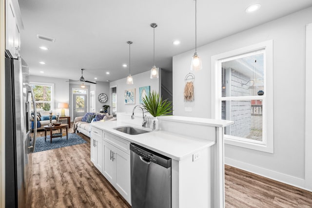 kitchen with sink, hanging light fixtures, stainless steel appliances, white cabinets, and a center island with sink